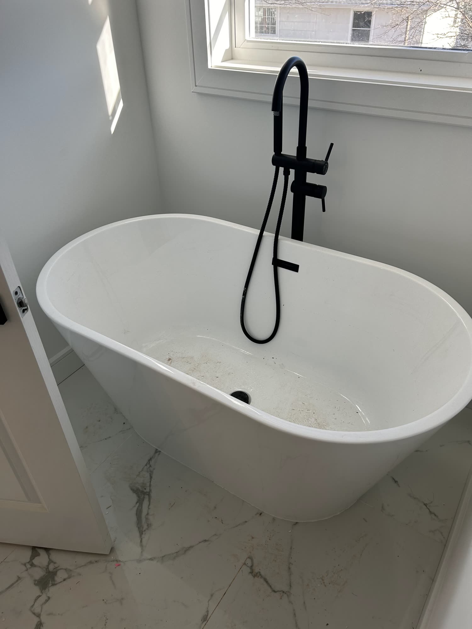 Freestanding white bathtub with matte black floor-mount faucet on marble tile